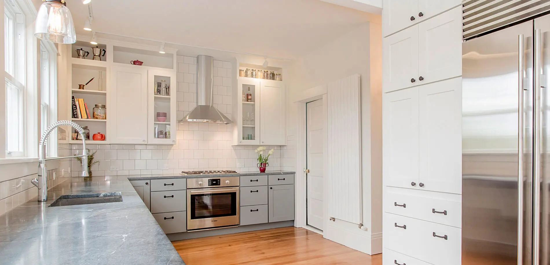 Modern kitchen with white cabinets, stainless steel appliances, gas stove, built-in oven, grey lower cabinets, and wood flooring—showcasing Greater Seattle custom home design at its finest.