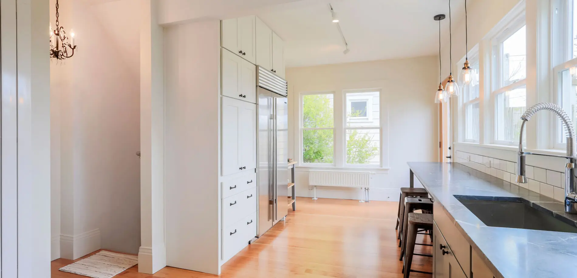 Bright kitchen with white cabinets, stainless steel appliances, black countertop, bar stools, large windows, and light wood floor—showcasing the elegance of Greater Seattle custom home design.