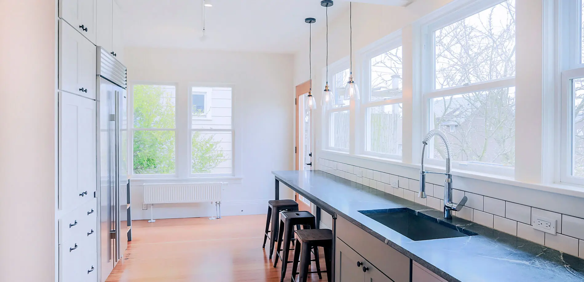 Bright modern kitchen with large windows, black countertop, pendant lights, bar stools, and white cabinets—an inspiring example of Greater Seattle custom home design.