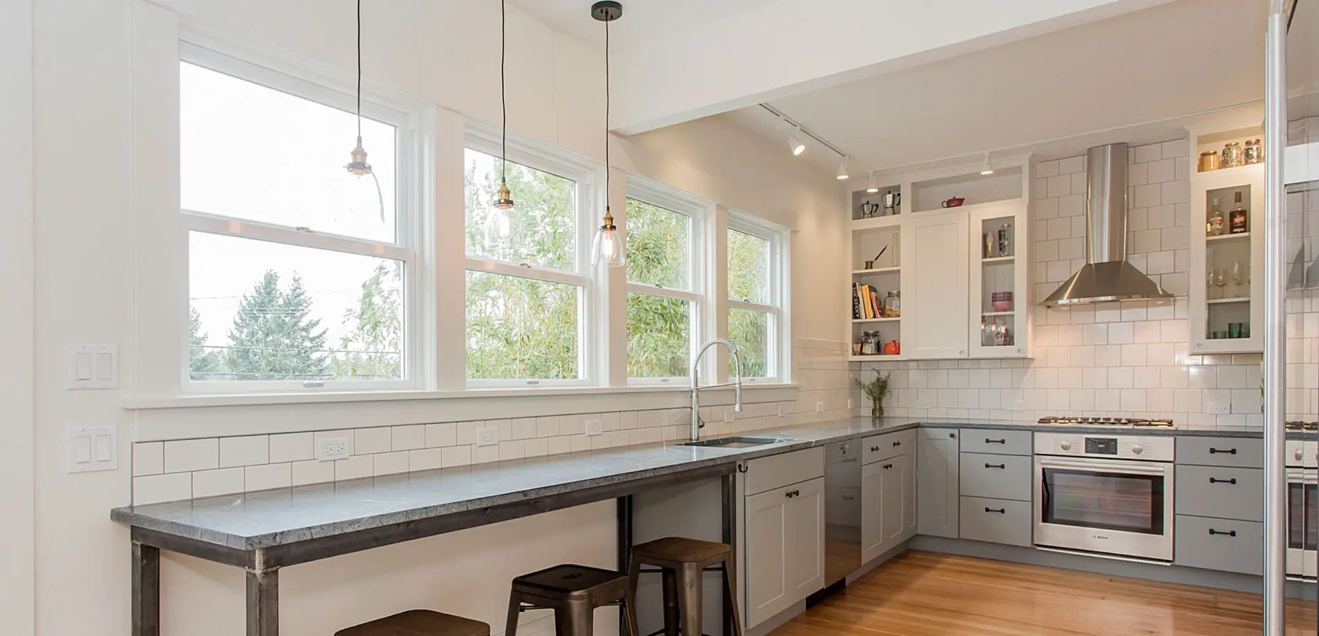 Modern kitchen remodels often feature white cabinets, stainless steel appliances, a long counter with bar stools, subway tile backsplash, and large windows letting in natural light.