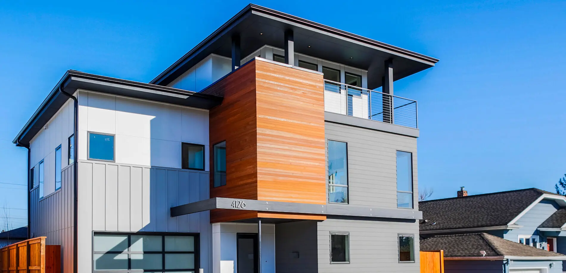 Modern two-story house with mixed gray, white, and wood panel siding, large windows, and a balcony under a flat roof—an elegant example inspired by Pacific Northwest residential architecture projects.