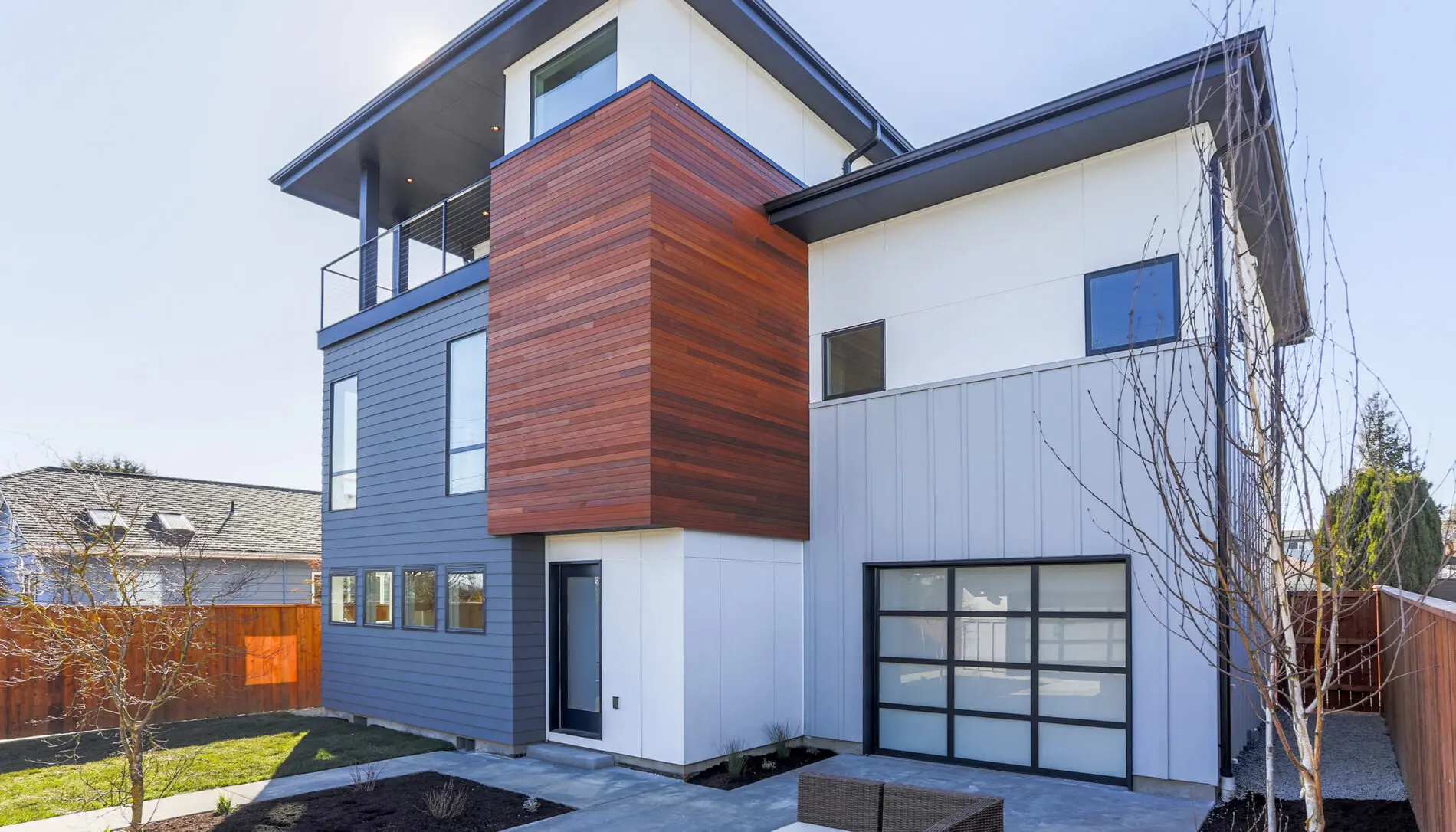 Modern two-story house with mixed wood and metal exterior, large windows, flat roof, attached garage, and minimalist landscaping—perfect for those seeking a sleek West Seattle custom home design.