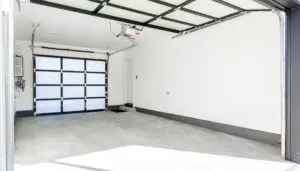 Empty, clean garage with white walls and concrete floor, featuring a glass-panel garage door—reflecting the modern touch of West Seattle custom home design. Ceiling-mounted opener and a door to the interior are visible.