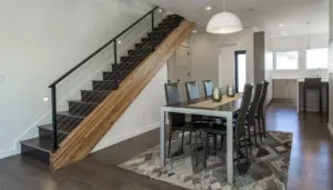 Modern dining area with a rectangular table and eight chairs, geometric rug, and staircase with wooden railing in an open-plan, well-lit West Seattle custom home design.