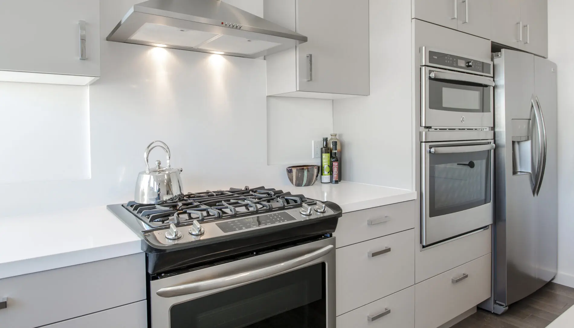 Modern kitchen with a gas stove, oven, stainless steel refrigerator, white cabinets, and a kettle on the stove—showcasing West Seattle custom home design at its finest.