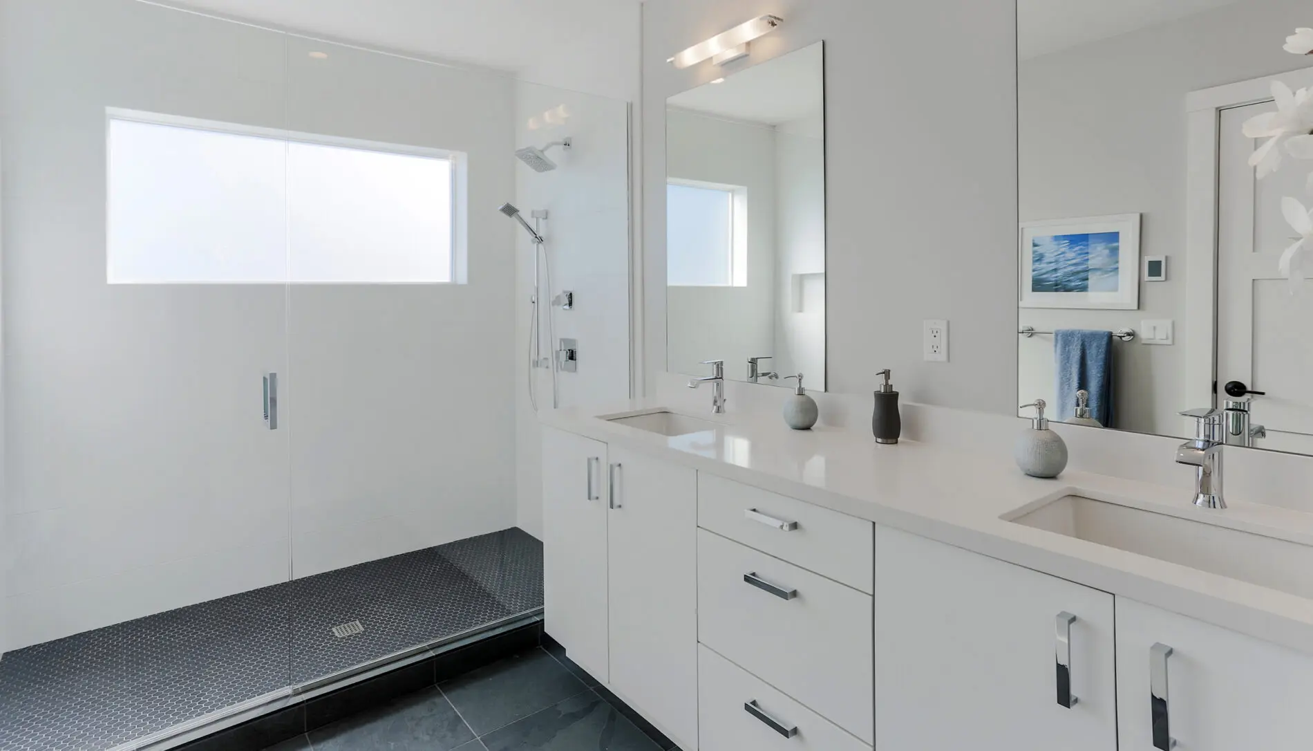 Modern bathroom with double sinks, white vanity, large mirrors, walk-in shower with glass doors, and minimal decor—showcasing the elegance of West Seattle custom home design.