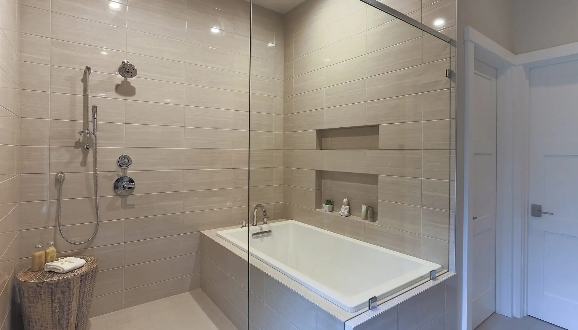 Modern bathroom with a built-in bathtub, wall-mounted shower, glass partition, and recessed shelves showcases Mercer Island custom home design. A basket with toiletries on the floor adds both function and style.
