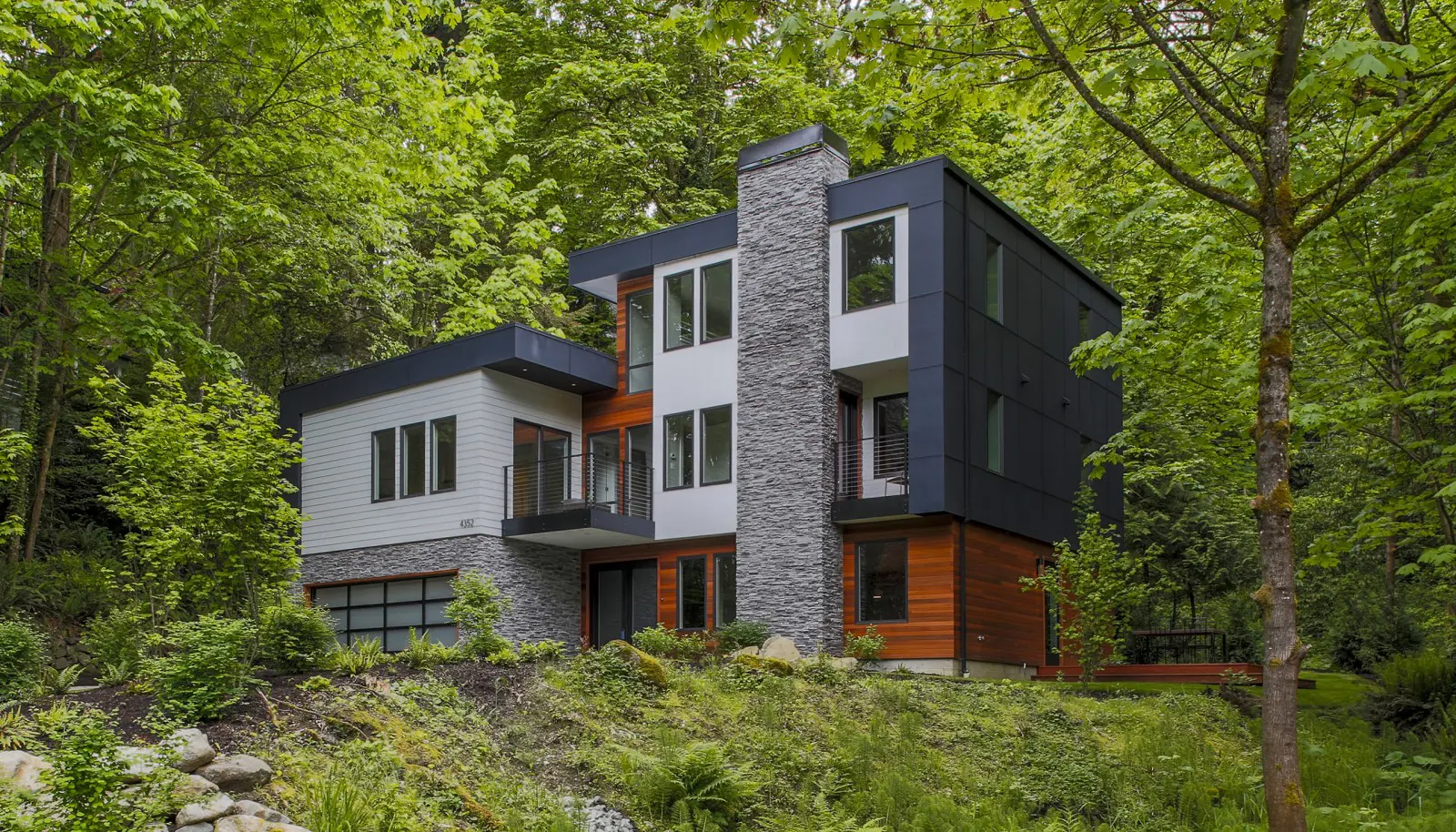 Modern two-story house with large windows, stone and wood exterior, surrounded by dense green trees—an elegant example of Pacific Northwest luxury residential architecture.