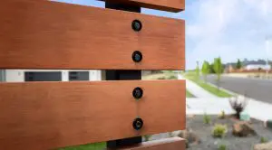 Close-up of horizontal wooden fence panels with metal bolts, set near a suburban street—an example of Walla Walla custom home design—accented by landscaped surroundings on a clear day.