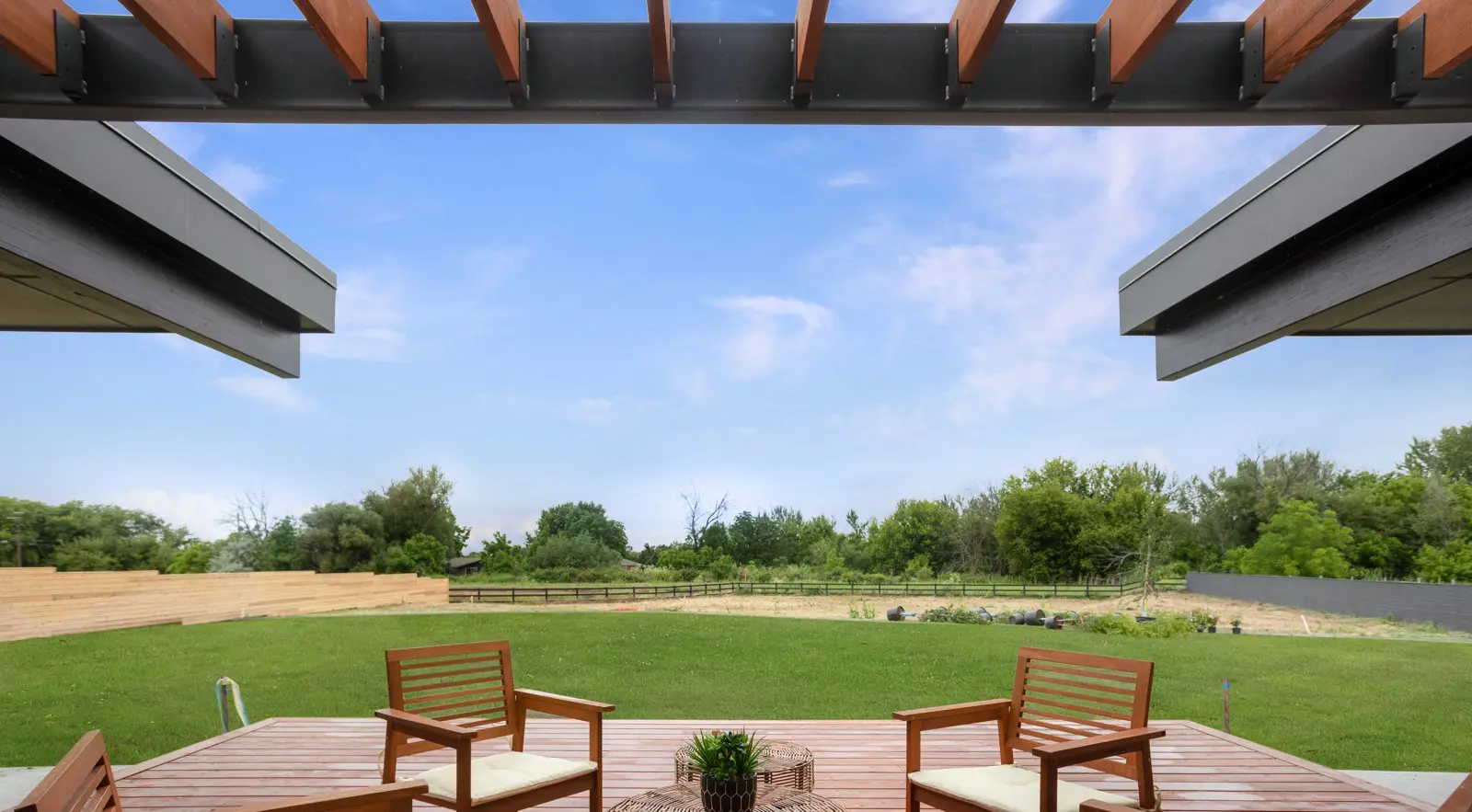 Enjoy the view from a covered patio with wooden chairs, overlooking a spacious green lawn and garden beds—showcasing thoughtful Walla Walla custom home design under a partly cloudy sky.