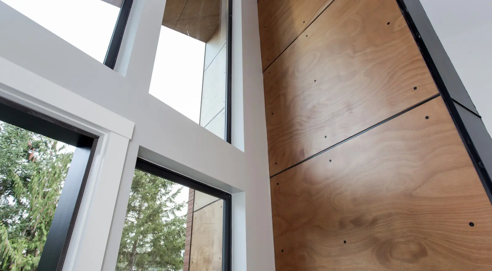 Tall windows with white frames and a wooden accent wall elevate this modern interior, showcasing Bellevue Meydenbauer custom home design, with views of trees just outside.