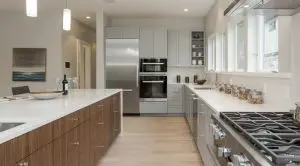 Modern kitchen with white countertops, wooden and gray cabinets, stainless steel appliances, and a gas stove—showcasing Bellevue Meydenbauer custom home design. Jars on the counter sit beneath a row of windows for added charm.