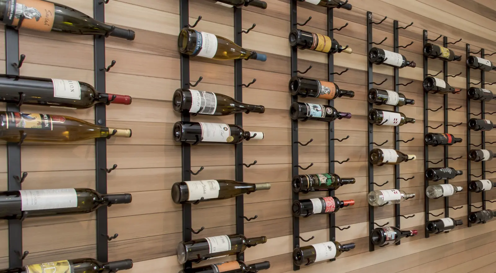 Bottles of wine displayed horizontally on a black metal rack mounted to a wooden wall, showcasing the elegance of Bellevue Meydenbauer custom home design.