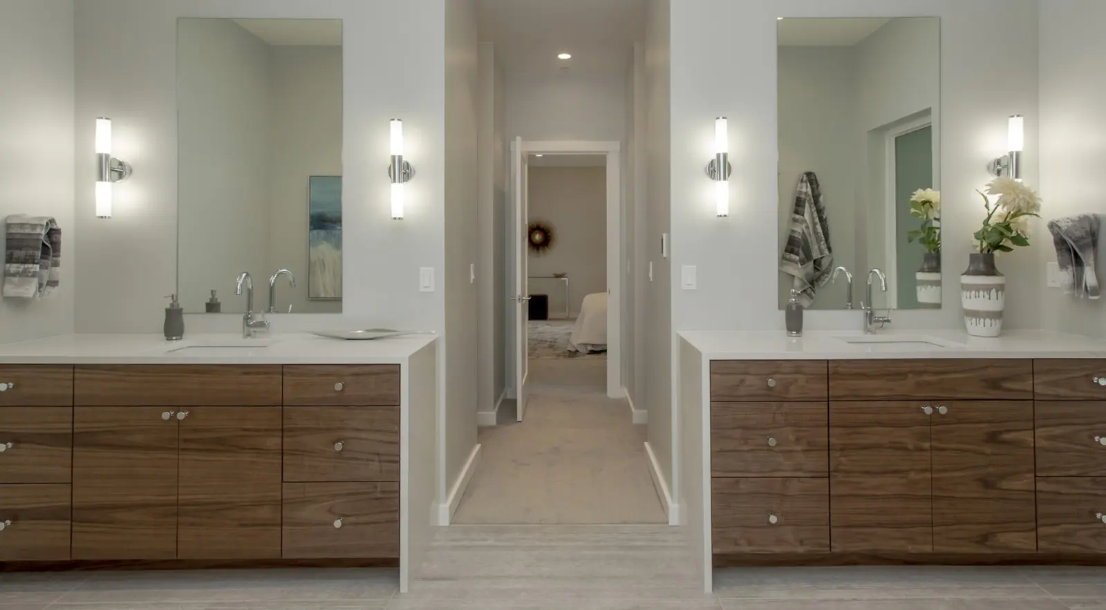 Modern bathroom in a Bellevue Meydenbauer custom home design, featuring two wooden vanities, large mirrors, wall-mounted lights, and a central walkway leading to the bedroom. Towels and decor accent the counters and walls.