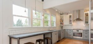Modern kitchen remodels often feature white cabinets, stainless steel appliances, a long counter with bar stools, subway tile backsplash, and large windows letting in natural light.
