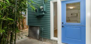 Blue door with glass window leads into a house with green siding; utility meter and bamboo plants are visible outside—an inviting example of Accessory Dwelling Units blending style and function.