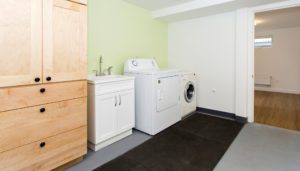 Laundry room with light green and white walls, light wood cabinets, a white sink, a washer, and a dryer, with an adjacent open doorway to another room with wood flooring.